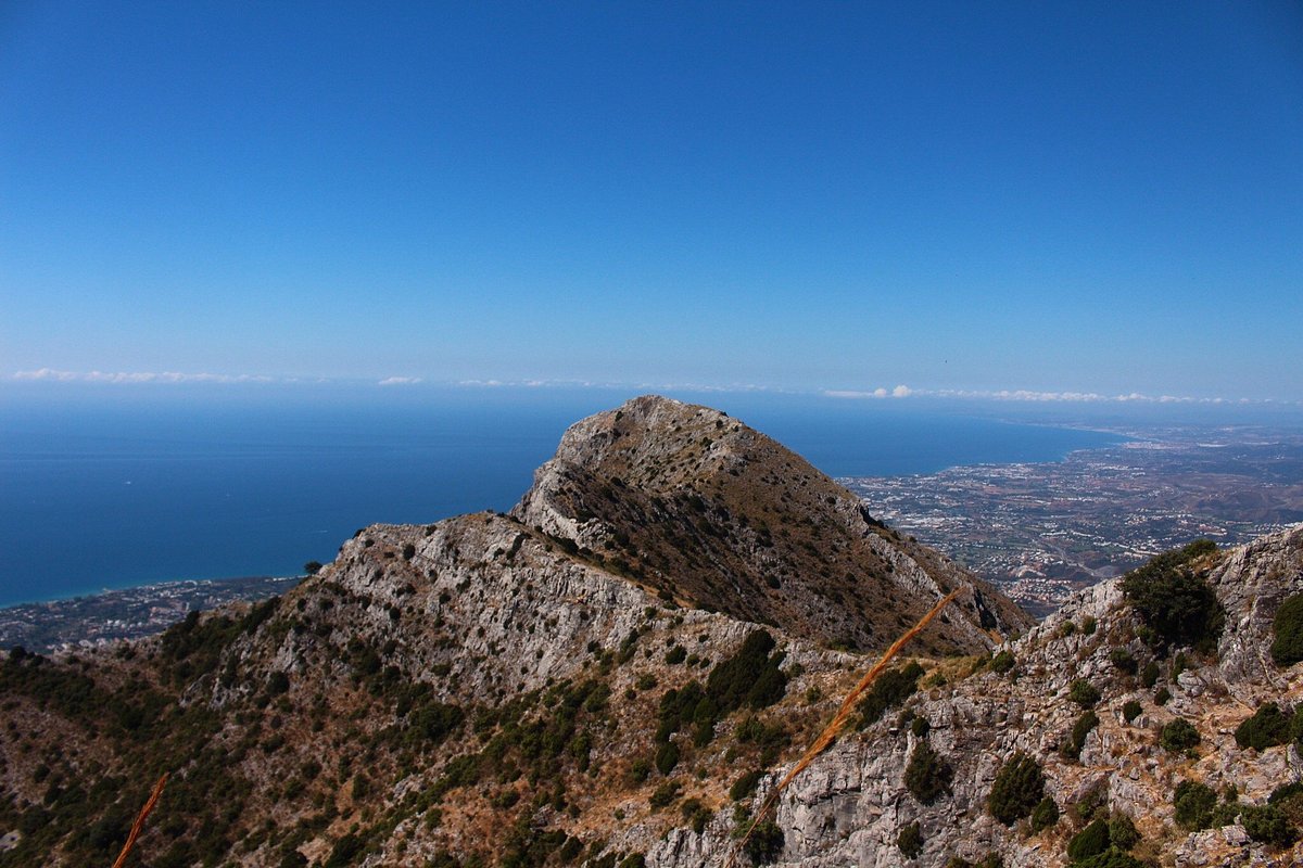 Hikers on a pine-forest trail in the Sierra Blanca above Marbella with limestone peaks and the Mediterranean in the distance
